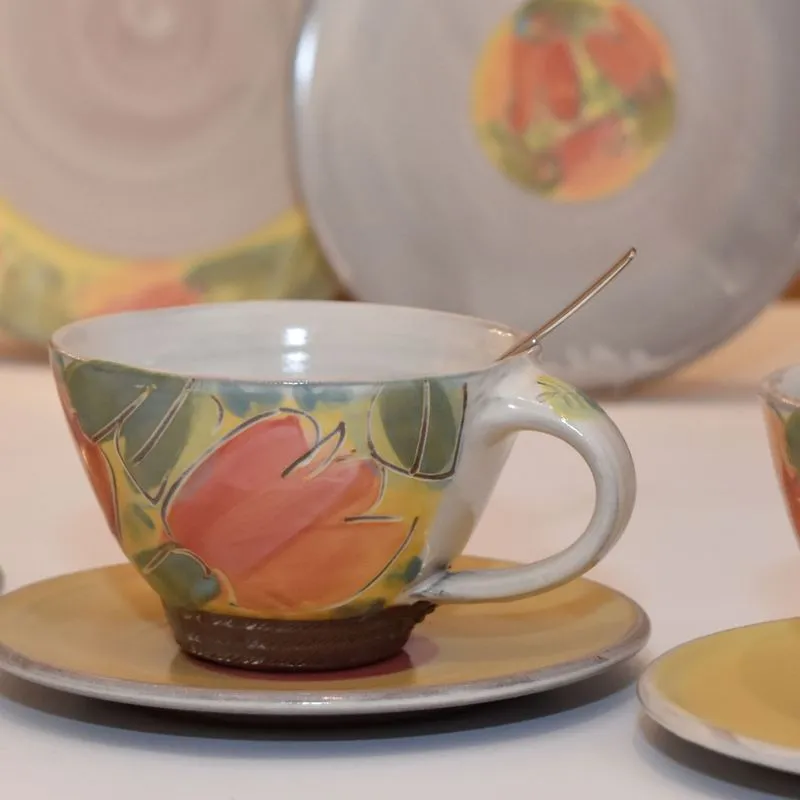 Handgetöpferte Keramik - Bauchige handgetöpferte Tasse aus Keramik im Blumendekor mit handgefertigtem Teller aus Keramik im Hintergrund.