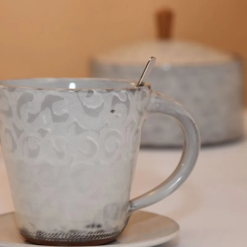 Handgetöpferte Keramik - Handgetöpferte Tasse aus Steinzeug Keramik in weiß mit handgefertigter Dose aus Keramik im Hintergrund.