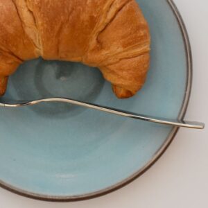 Handgetöpferter Unterteller aus Keramik in blau mit einem Croissant und einer Gabel auf dem Teller.